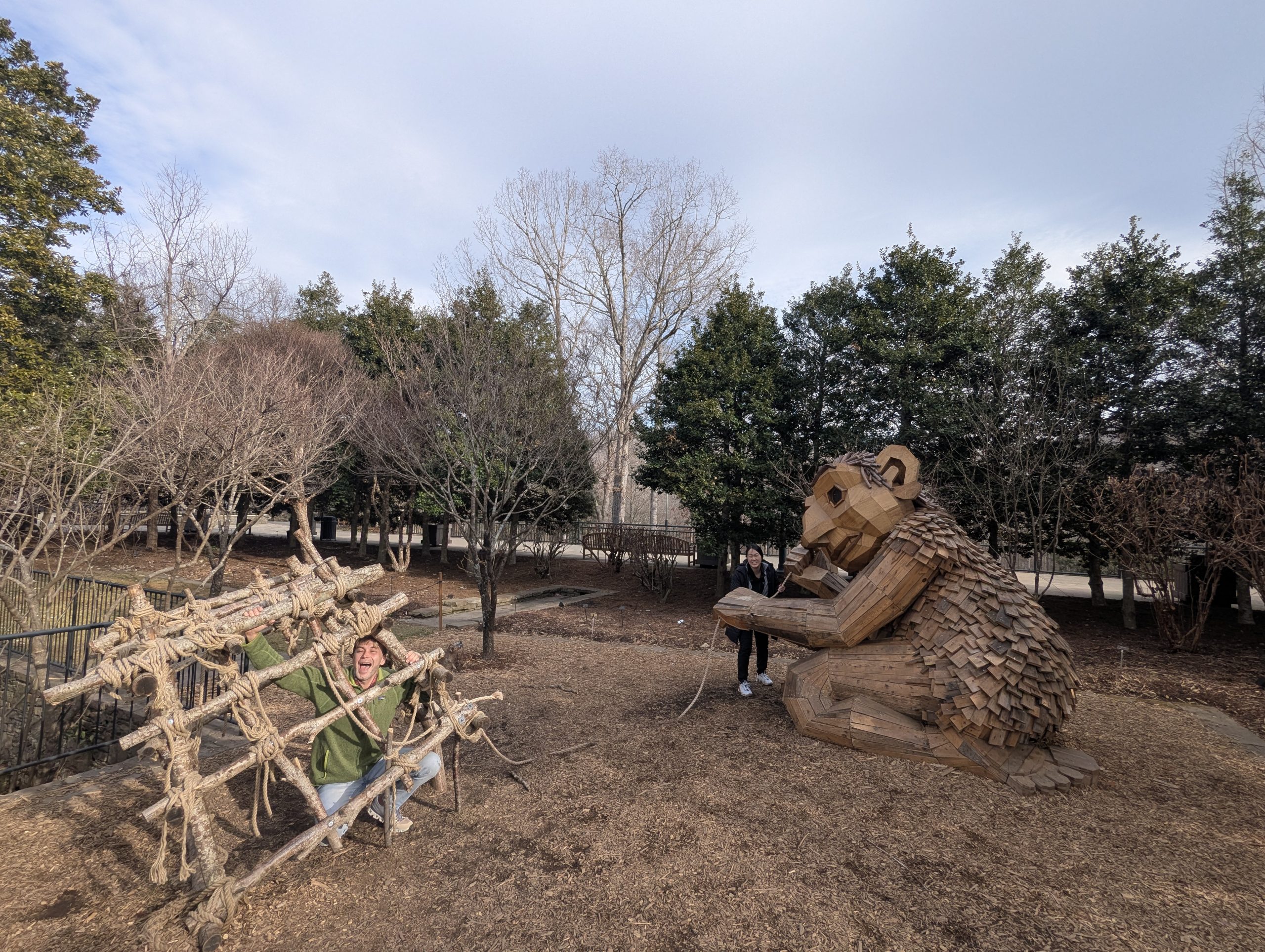 Picture of a larger than lifesize troll and a larger than lifesize wooden trap with a man in the trap and a woman standing beside the troll