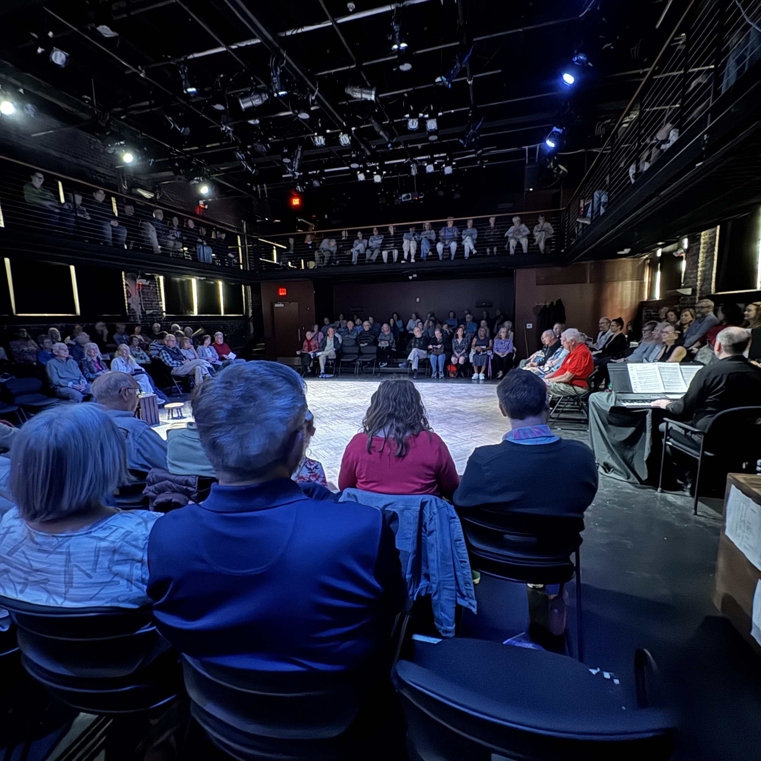 A group of people sitting in a darkened theater arranged in the round
